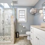 Light blue modern bathroom interior with glass door shower and white cabinet with mirror